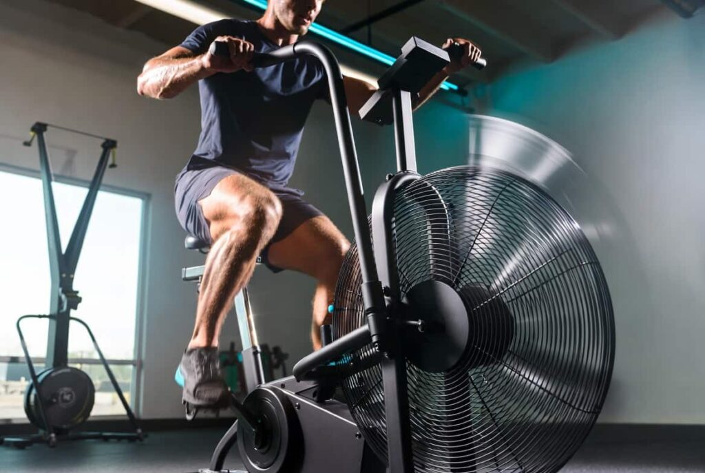 Athlete performing a high intensity workout on an air bike, also known as an assault bike, in a gym